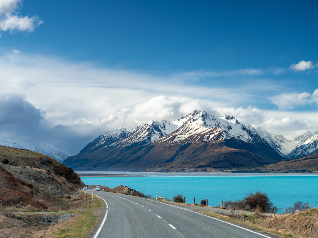Scenic view at Mount Cook Road alongside Lake Pukaki with snow capped Southern Alps basking in the late winter evening light. Best road trip route in New Zealand South Island.